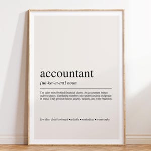 May include: A framed wall art print featuring a dictionary-style definition of the word accountant. The text is printed in black on a light beige background, including the phonetic pronunciation, noun classification, and a descriptive paragraph.