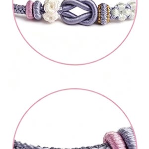 May include: A lavender cord bracelet featuring a central infinity knot, accented with small white floral-shaped knots, pink cylindrical beads, and a gold-toned textured bead. The cord is constructed from a braided lavender thread material.
