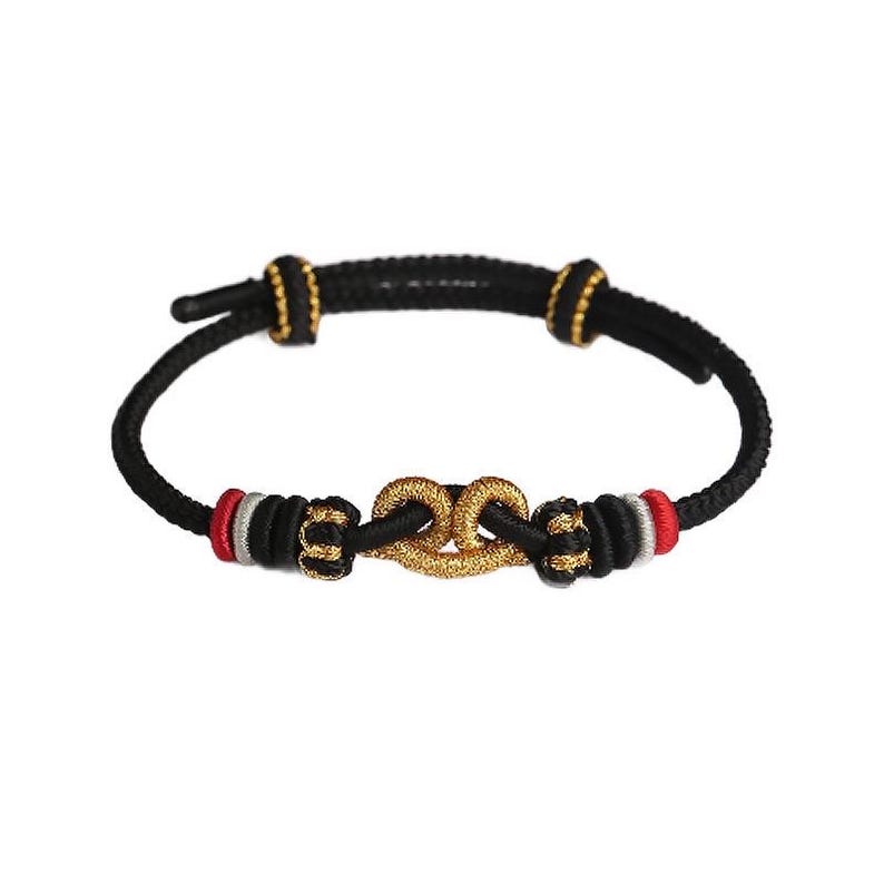 May include: A black cord bracelet featuring a central gold-colored knot ornament. The bracelet is accented with small gold-colored beads, red and silver thread detailing, and adjustable sliding knots for a secure fit on the wrist.