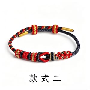 May include: A braided cord bracelet featuring black, red, and gold threads woven into a complex pattern with a central knot and adjustable sliding components. The text "款 式 二" is printed below the bracelet on a plain white background.
