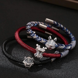 Puede incluir: Tres pulseras con abalorios plateados con forma de animales. Una pulsera es negra, otra roja y la otra azul y blanca. Las pulseras están hechas de cordón tejido y tienen cierres plateados.