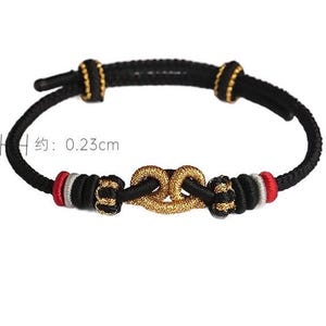 May include: A black cord bracelet featuring a central gold-colored knot, accented with red, silver, and black thread details. The cord has a thickness of 0.23 cm as indicated by the visible measurement text. The design includes two sliding knots for adjustment.