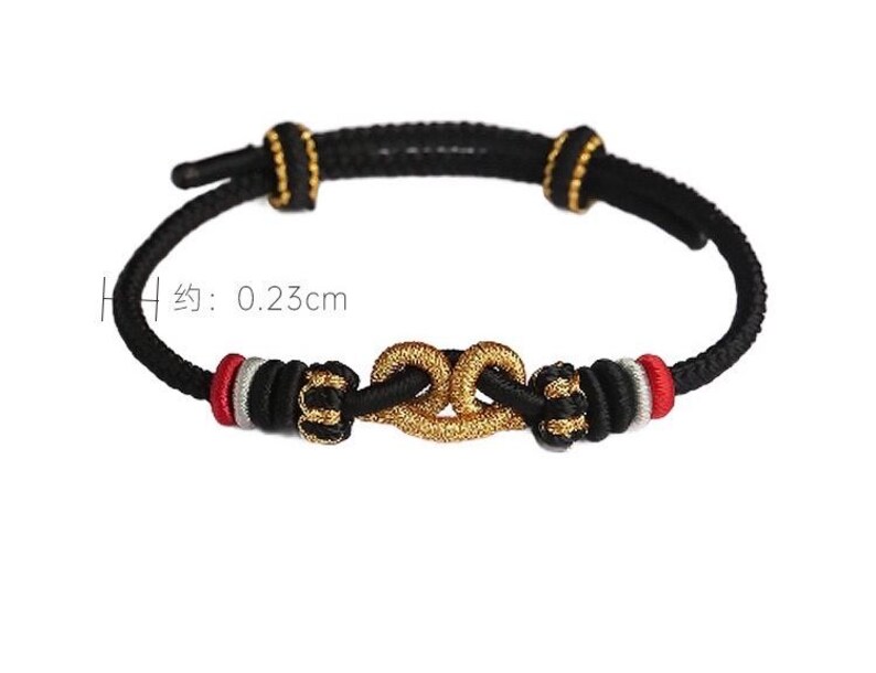 May include: A black cord bracelet featuring a central gold-colored knot, accented with red, silver, and black thread details. The cord has a thickness of 0.23 cm as indicated by the visible measurement text. The design includes two sliding knots for adjustment.