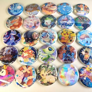 May include: A collection of 25 round, colorful buttons featuring various Pokemon characters. The buttons are arranged in a grid pattern on a white surface.