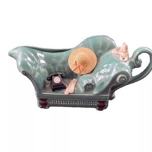 May include: A green ceramic couch shaped serving dish with a straw hat, a phone, and a small cat figurine.