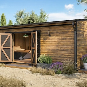 Op de afbeelding: Een kleine houten hut met open dubbele deuren die een slaapkamer onthullen. De buitenkant heeft een verweerde houten afwerking, zwarte afwerking en decoratieve verlichting. Lavendel en andere planten staan in plantenbakken buiten. Een witte parasol en houten stoel staan aan de zijkant.