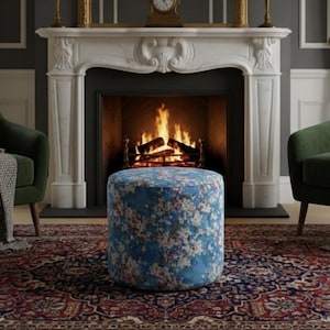 May include: A living room with a fireplace, two green armchairs, and a blue floral ottoman. The fireplace has a burning fire, a gold mirror, and a clock. The ottoman sits on a patterned rug, creating a warm atmosphere.