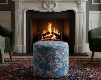 Pode incluir: Uma sala de estar acolhedora com lareira e fogo. Duas poltronas verdes ladeiam um pufe azul com estampa floral. Um espelho dourado e um relógio adornam a lareira, tudo sobre um tapete estampado.
