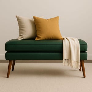 May include: A green bench with wooden legs, topped with two square pillows in beige and mustard yellow. A cream-colored throw blanket with fringe is draped over the bench.