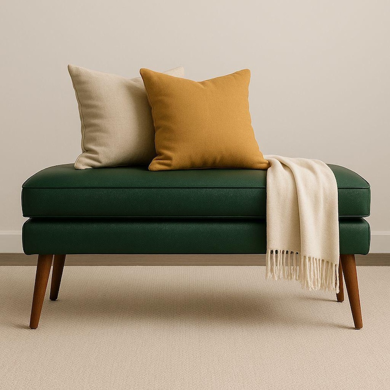 May include: A green bench with wooden legs, topped with two square pillows in beige and mustard yellow. A cream-colored throw blanket with fringe is draped over the bench.