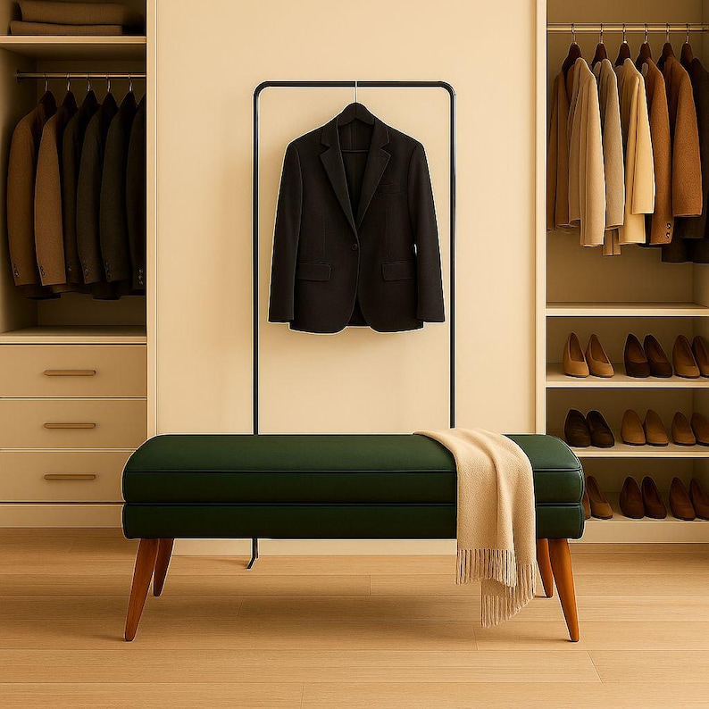 May include: A dark green upholstered bench with wooden legs and a beige throw blanket. A black blazer hangs on a black clothing rack. Closets with suits and shoes are in the background.