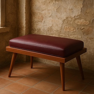 Puede incluir: Un banco de madera con un asiento de cuero burdeos y cuatro patas. El banco est&aacute; en una habitaci&oacute;n con una pared de piedra en el fondo.