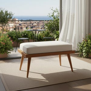 May include: A wooden bench with a white cushion on a patio. The bench has angled legs and a rectangular seat. The background shows a cityscape, plants, and a table with chairs.