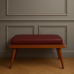 Puede incluir: Un banco de madera con un asiento de cuero rojo. El banco tiene un dise&ntilde;o sencillo con cuatro patas y un asiento rectangular.