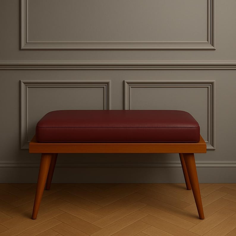 Puede incluir: Un banco de madera con un asiento de cuero rojo. El banco tiene un dise&ntilde;o sencillo con cuatro patas y un asiento rectangular.