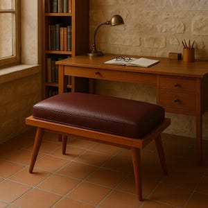 Puede incluir: Un banco de madera con un asiento de cuero burdeos. El banco tiene un dise&ntilde;o sencillo con cuatro patas y una parte superior rectangular. El banco est&aacute; en una habitaci&oacute;n con un escritorio de madera y una estanter&iacute;a.