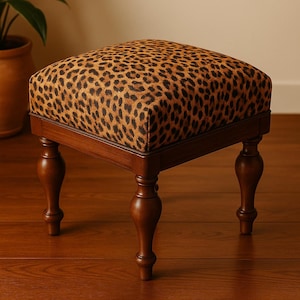 Puede incluir: Un taburete de madera marrón con cuatro patas torneadas y un asiento cuadrado con estampado de leopardo.