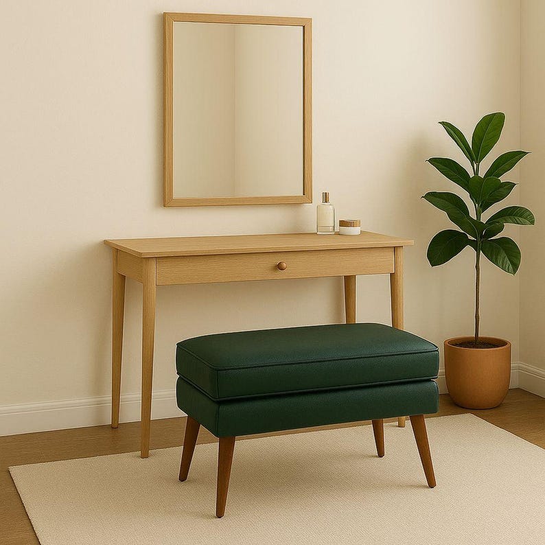 May include: A light wood vanity table with a rectangular mirror, a dark green upholstered bench, and a potted plant. The bench has wooden legs. The vanity has a single drawer and a small bottle and jar on top.