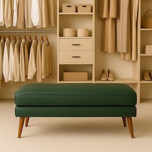 May include: A dark green upholstered bench with wooden legs is centered in front of a closet filled with clothing. The bench has a rectangular shape and a tufted design. The closet features shelves, drawers, and hanging clothes in neutral tones.