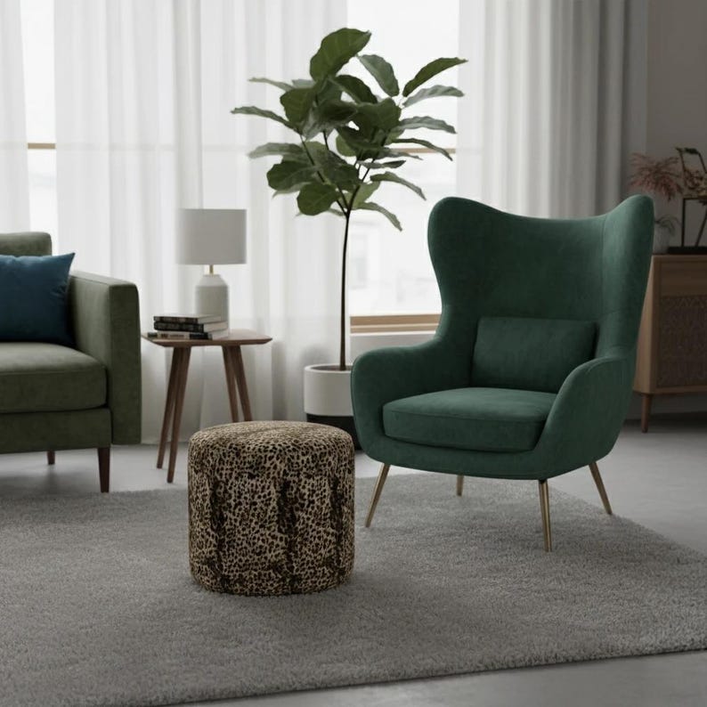 May include: A living room scene featuring a green armchair with a matching pillow, a green sofa, and a leopard-print ottoman. A small side table with a lamp and a potted plant are also visible. The room has a neutral color palette with a gray rug.