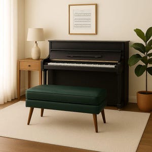 May include: A dark green upholstered bench with wooden legs sits in front of a black piano. A framed musical score hangs on the wall above the piano. A wooden side table with a lamp and a potted plant are also in the room.