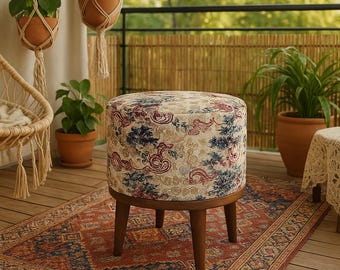 Könnte beinhalten: Ein runder, gemusterter Hocker mit Holzbeinen. Der Hocker hat einen cremefarbenen Hintergrund mit einem Blumendesign in Blautönen, Rot und Gold. Der Hocker steht auf einem Teppich mit einem ähnlichen Muster.