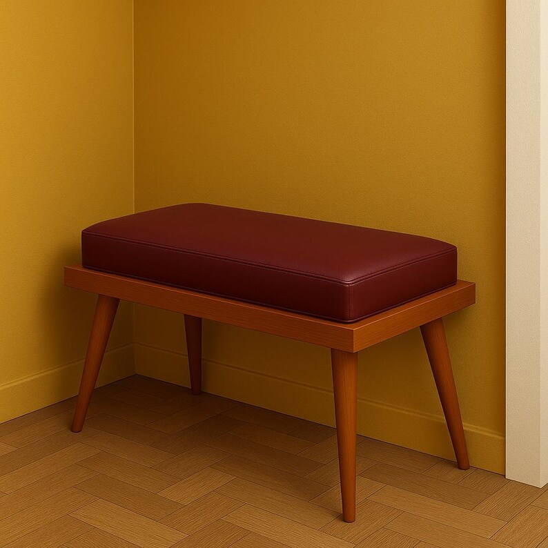 Puede incluir: Un banco de madera con un asiento tapizado de color burdeos. El banco tiene cuatro patas y est&aacute; en una esquina de una habitaci&oacute;n con paredes amarillas.