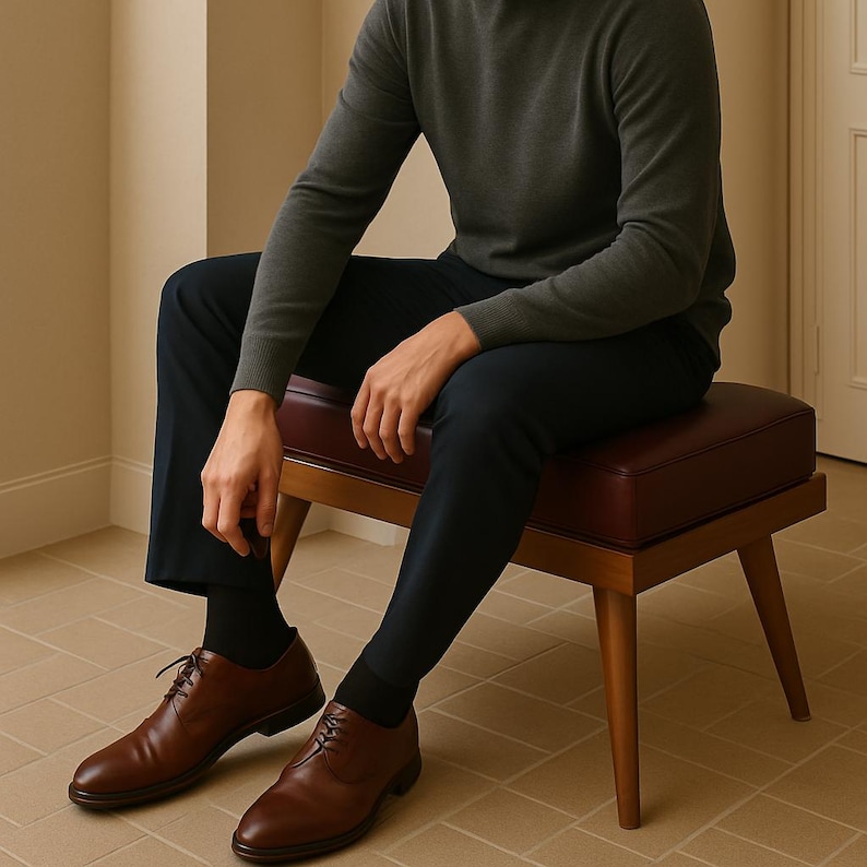 Puede incluir: Una persona con un su&eacute;ter verde oscuro y pantalones azul oscuro se sienta en un taburete de madera con un coj&iacute;n burdeos. Lleva zapatos marrones de cuero con cordones.