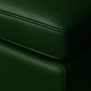 May include: Close-up of a section of a dark green leather surface. The leather has a textured appearance with visible stitching along the edges, suggesting a piece of furniture or upholstery.