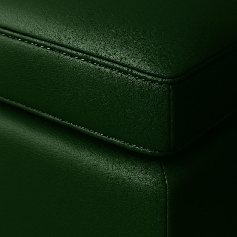 May include: Close-up of a section of a dark green leather surface. The leather has a textured appearance with visible stitching along the edges, suggesting a piece of furniture or upholstery.
