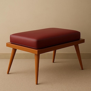 Puede incluir: Un reposapi&eacute;s de madera con un coj&iacute;n de cuero rojo. El taburete tiene cuatro patas y una parte superior rectangular.