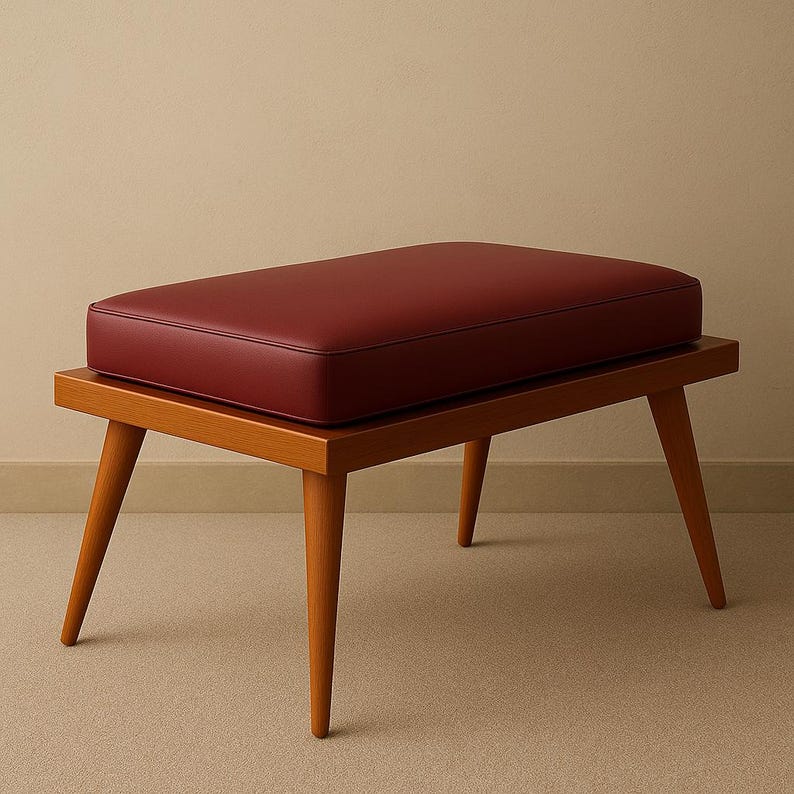 Puede incluir: Un reposapi&eacute;s de madera con un coj&iacute;n de cuero rojo. El taburete tiene cuatro patas y una parte superior rectangular.