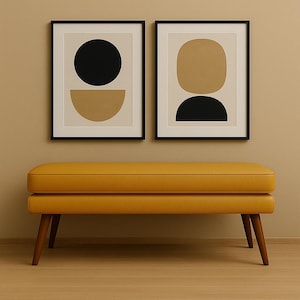 May include: A mustard yellow bench with wooden legs sits below two framed abstract art prints. The prints feature black and tan geometric shapes on a cream background. The bench has a rectangular shape and a padded top.