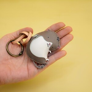 May include: A brown and white leather keychain shaped like a cat with a key ring attached.