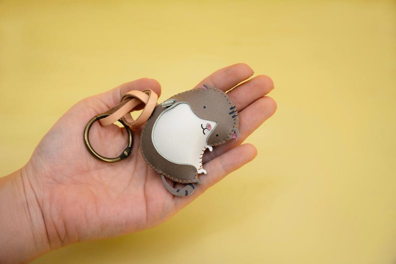May include: A brown and white leather keychain shaped like a cat with a key ring attached.