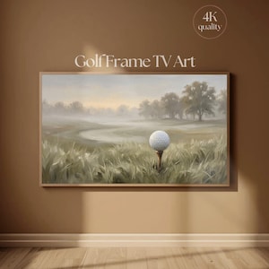 Puede incluir: Un marco digital rectangular que muestra una pintura de paisaje de una pelota de golf blanca sobre un tee en hierba alta. El fondo presenta un campo de golf brumoso con árboles bajo un cielo suave. El texto Golf Frame TV Art y 4K quality son visibles.