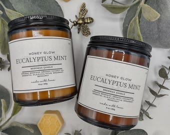 May include: Two glass jars of Eucalyptus Mint beeswax candles with black lids and white labels. The labels read "Honey Glow Eucalyptus Mint". The image includes a gold bee figurine and two honeycomb-shaped wax melts. The candles are 6 oz / 250g.