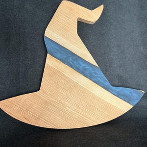 Puede incluir: Una tabla de cortar de madera con forma de sombrero de bruja con una incrustación de resina azul.
