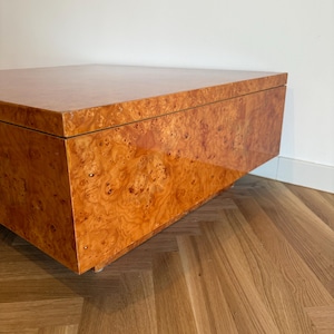 May include: A large, rectangular wooden cabinet with a glossy, burl wood finish. The cabinet is a warm, reddish-brown colour with a unique, swirling grain pattern. The design is modern and minimalist, with clean lines and a floating appearance.
