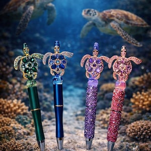 May include: Four decorative pens with turtle-shaped tops, each adorned with colourful gemstones. The pens are in shades of green, blue, purple, and red, with a silver tip. The background features two sea turtles and an underwater scene.