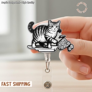 May include: A black and white cat badge reel with a striped pattern, holding a container of ice cubes. The reel has the text "Arcylic Badge Reel - High Quality" and "Novel Badge Store". The reel is attached to a clear plastic holder.