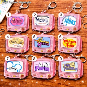 May include: A collection of pink acrylic keychains shaped like retro televisions. Each keychain features a different Disney show logo, including "Lizzie McGuire," "Wizards of Waverly Place," and "Hannah Montana." The keychains have silver-colored hardware.