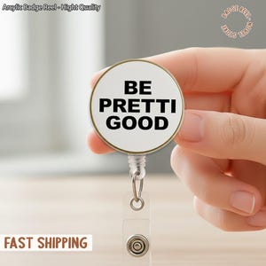 Pode incluir: Um crachá branco e dourado com o texto "BE PRETTI GOOD" em preto. O crachá tem uma alça de plástico transparente e um clipe de metal. As palavras "Arcylic Badge Reel - Hight Quality" estão no topo.