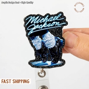 May include: A black glitter badge reel featuring a neon blue image of Michael Jackson. The badge reel has a clear plastic strap and a metal clip. The text "Michael Jackson" is written in a neon blue font. The words "Arcylic Badge Reel - High Quality" are at the top.