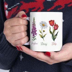 May include: White ceramic mug with a floral design featuring a foxglove, daisy, and tulip. The flowers are illustrated in watercolor style and labeled with their names.