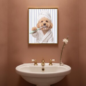 Puede incluir: Una lámina de arte enmarcada que muestra a un caniche marrón claro con un albornoz blanco y una toalla a juego en la cabeza. El perro sostiene un cepillo de dientes eléctrico verde claro en la pata, con espuma de pasta de dientes blanca.