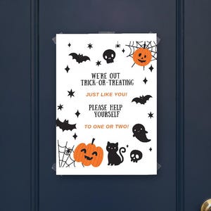 May include: A white rectangular sign with black and orange Halloween graphics including pumpkins, bats, a cat, a ghost, skulls, and spiderwebs. The text reads: WE'RE OUT TRICK-OR-TREATING JUST LIKE YOU! PLEASE HELP YOURSELF TO ONE OR TWO!