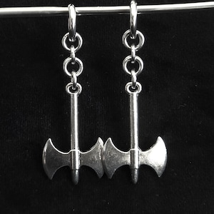 May include: Silver-toned axe earrings. Each earring features a small axe pendant suspended from a series of linked rings and a hoop. The axes have a double-bladed design and are displayed against a black background.