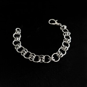 May include: A silver-toned chainmail bracelet constructed from a series of interlocking circular metal rings. The bracelet features a polished finish and is secured with a lobster claw clasp at one end, forming a continuous, flexible circular link design.