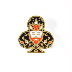 May include: A black and gold enamel pin shaped like a clover with a stylized face in the center. The face has a white beard and a red flower on its head.